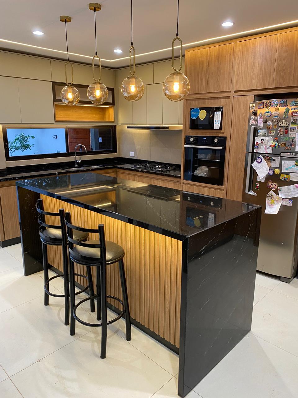 Cocina terminada de la vivienda C y A, con isla de mármol negro, muebles de madera y lámparas colgantes